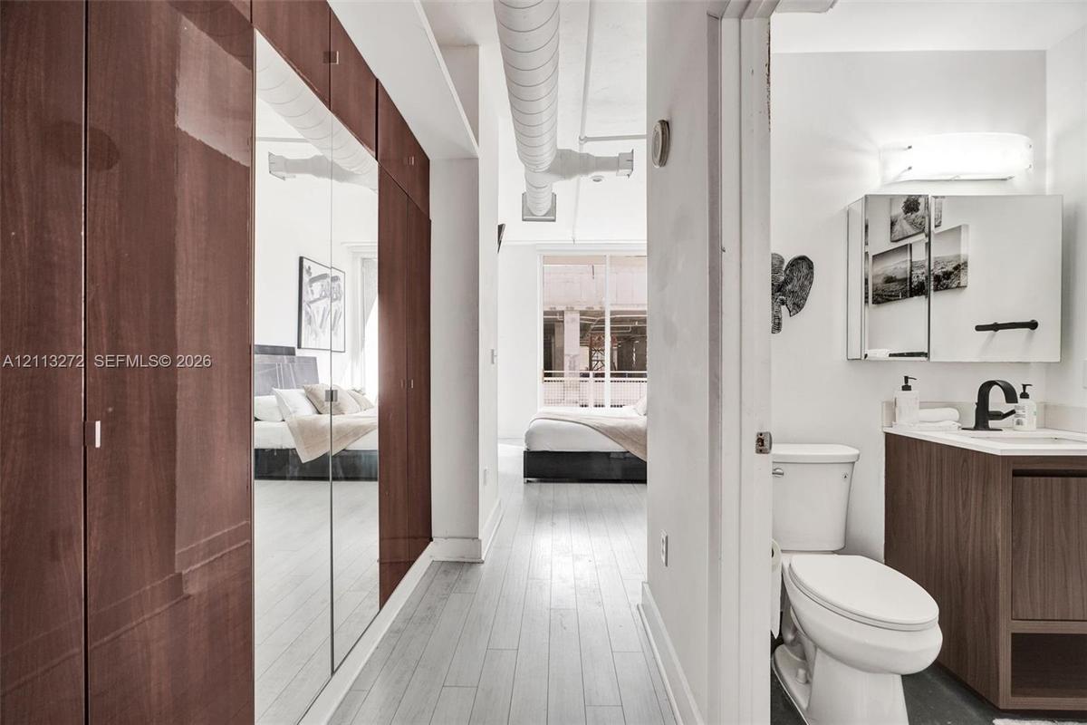 Floor-to-ceiling cabinetry with mirrored doors, wood-finish flooring, industrial exposed ductwork, and vanity with an integrated sink and matte black 