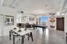 Open-concept interior featuring light wood-finish flooring, exposed industrial-style ceiling ductwork, floor-to-ceiling windows, and a dark wood barn-