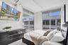 Floor-to-ceiling windows, sliding glass door with access to a balcony, high ceilings with exposed conduits, and light wood-finish flooring