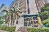 Multi-story high-rise exterior featuring concrete balconies, floor-to-ceiling glass-paneled ground-level entryway, decorative blue architectural awnin