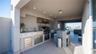 Covered outdoor kitchen featuring a built-in stainless steel grill, range hood, stone countertop with integrated sink, and stainless steel under-count