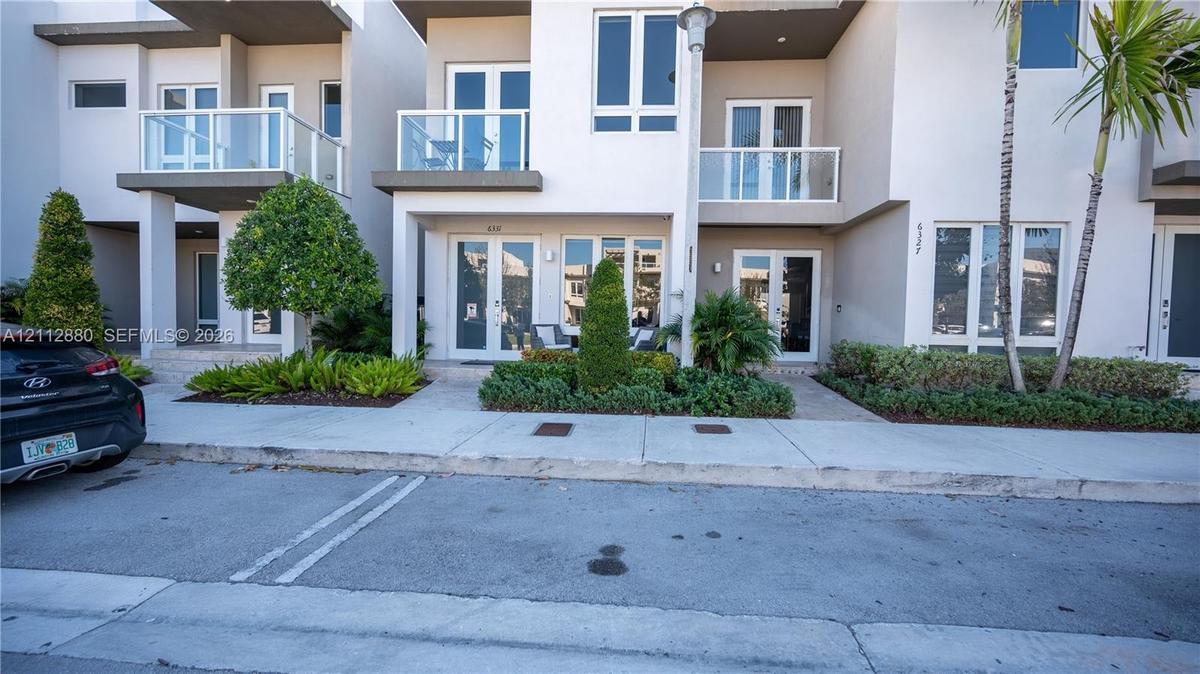 Contemporary multi-story exterior featuring smooth stucco facade, glass-paneled balconies, French-style entry doors, and professional landscaping