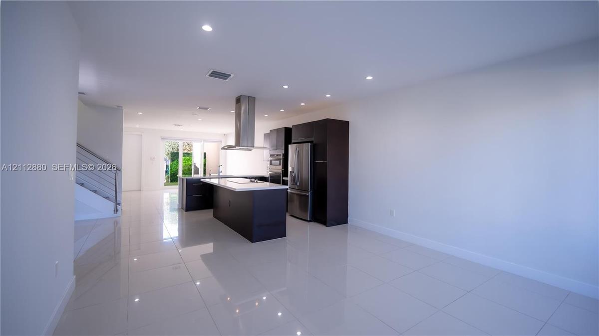 Modern kitchen featuring dark cabinetry, a central island with a stone-finish countertop, recessed lighting, polished tile flooring, and a stainless s