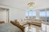 Floor-to-ceiling windows, polished stone flooring, intricate crown molding, and decorative ceiling medallion with a tiered glass chandelier
