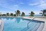 Swimming pool with mosaic tile border, light-toned stone decking, metal handrail, and transparent glass railing overlooking the ocean