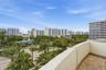 Balcony with textured masonry walls and tiled flooring overlooking an urban landscape featuring mature palm trees and multi-story structures