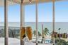 Floor-to-ceiling windows featuring panoramic oceanfront exposure, exterior balcony with railing, and integrated overhead lighting fixture