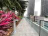 Terrace featuring large-format stone-look tile flooring, glass panel railing, and integrated metal path lighting, bordered by mature palm trees and tr