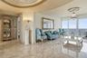 Polished stone flooring, recessed tray ceiling with gold-tone molding, crystal chandelier, and floor-to-ceiling glass sliding doors with ocean backdro