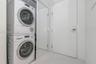 Stacked Bosch laundry center enclosed by sliding mirrored doors, set against large-format tile flooring and a solid-core door featuring electronic key
