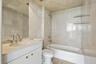 Full-height stone tile wall treatments, integrated floating stone shelving, undermount sink with polished chrome hardware, custom white cabinetry with