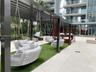 Outdoor common area featuring a black metal pergola, integrated artificial turf flooring, built-in tiered wood-tone seating, and suspended seating str