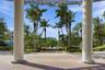 Covered entrance featuring structural columns and a paver stone patio, centered fountain, and mature palm landscaping