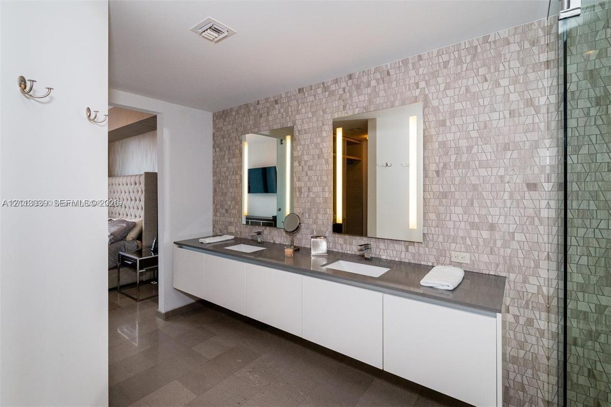 Floating dual-sink vanity with a solid surface countertop, mosaic tile backsplash, integrated rectangular sinks, and wall-mounted mirrors with built-i