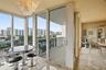 Floor-to-ceiling glass paneling, sliding glass door access to a private balcony, polished stone-finish flooring, and a decorative crystal chandelier