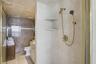 Walk-in shower enclosure featuring floor-to-ceiling neutral tile, built-in shelving, and gold-finish hardware including a handheld showerhead