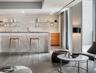 Stone-surfaced kitchen island with waterfall edge, wood-finish flooring, custom wood-tone cabinetry, and tiered glass shelving