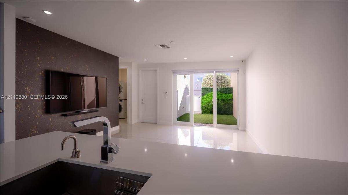 Open-concept interior featuring a solid-surface kitchen island, recessed lighting, white tile flooring, a textured accent wall, and sliding glass door