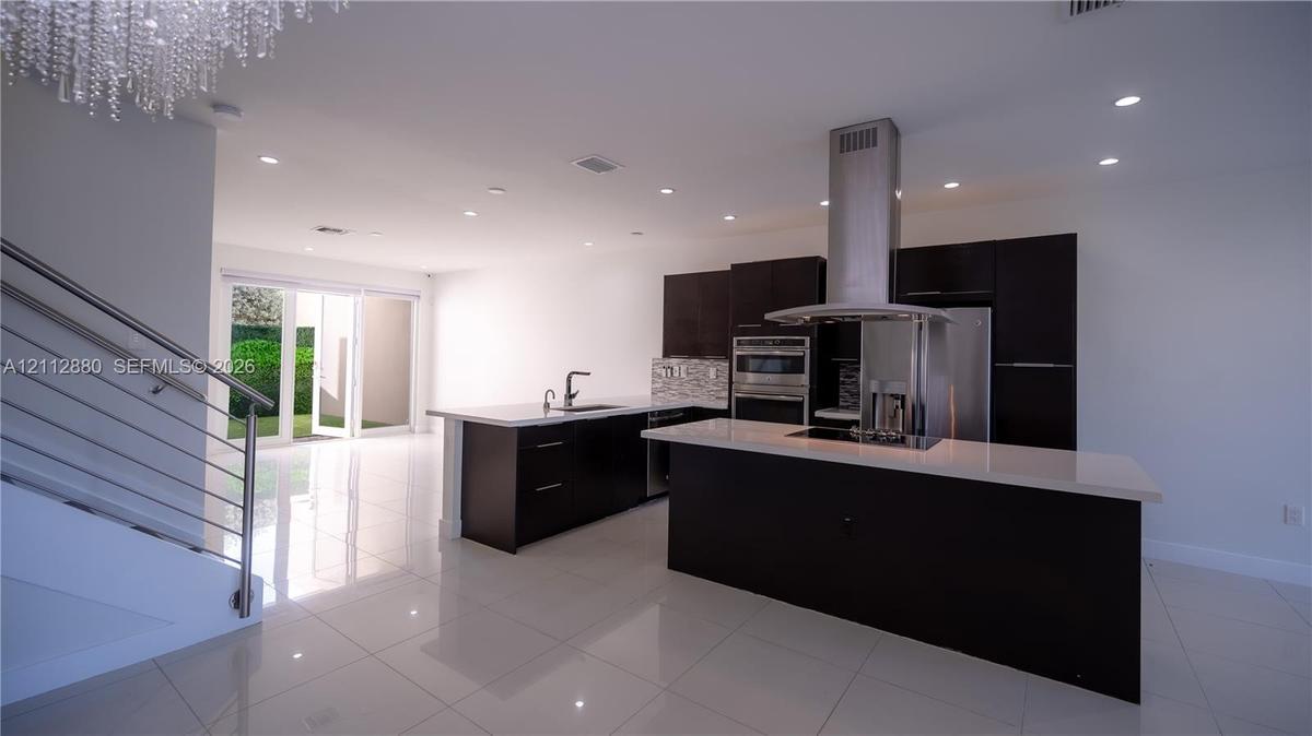 Kitchen featuring dark cabinetry, quartz countertops, a stainless steel range hood, built-in wall oven, and polished tile flooring