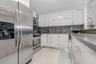 Kitchen featuring high-gloss white cabinetry, stainless steel appliances, solid-surface countertops, a gooseneck faucet, and white tile flooring