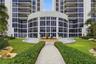 High-rise exterior featuring a multi-story glass facade, private balconies, a central water fountain, stone-paved pathways, and manicured landscaping