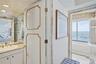 Vanity featuring an oval undermount sink, stone countertop, and full-height mirrored wall, paired with a jetted soaking tub positioned against a large