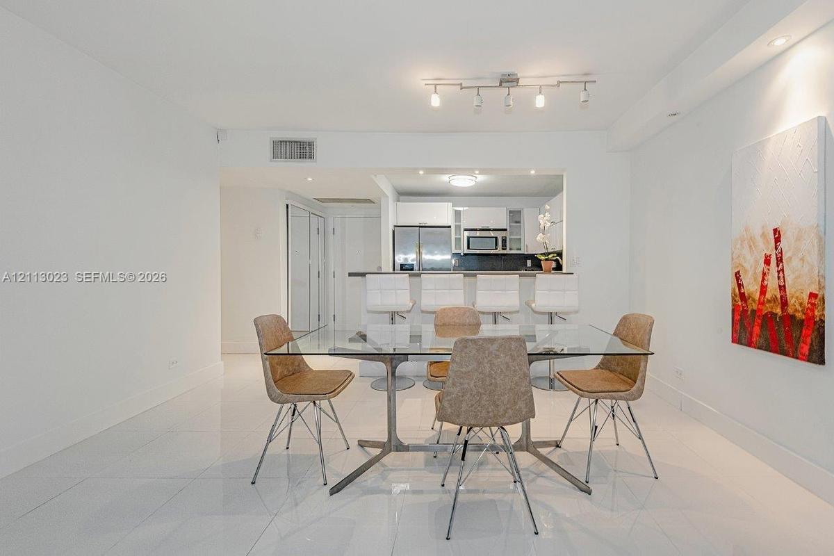 Polished tile flooring, neutral wall finishes, track lighting, and a kitchen pass-through with an integrated breakfast bar