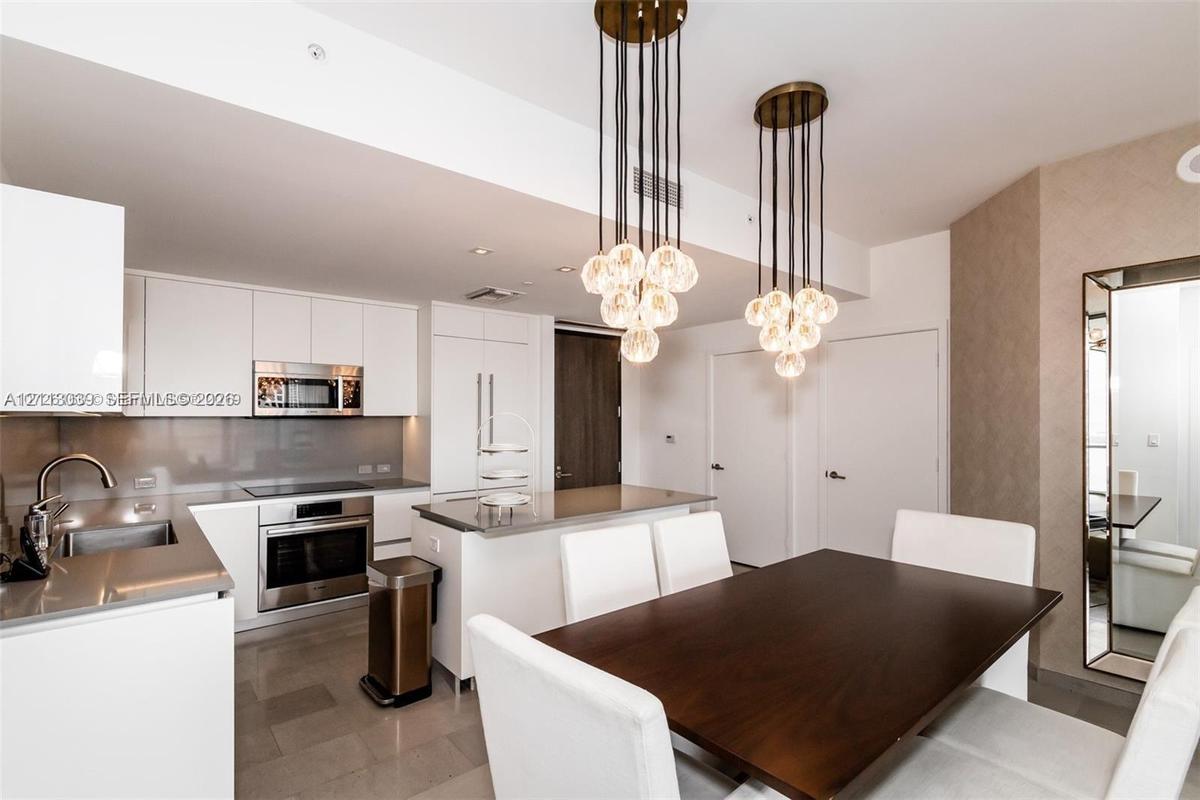 Contemporary kitchen featuring white flat-panel cabinetry, stainless steel appliances, a flush-mount electric cooktop, quartz countertops, and dual mu