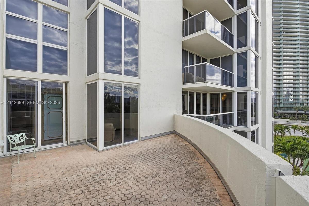 Expansive private balcony featuring patterned paver flooring, floor-to-ceiling glass paneling, and glass-paneled railings