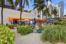 Outdoor patio area featuring a retractable orange awning, sandy ground surface, mature palm trees, and native coastal vegetation