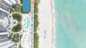 Aerial perspective of a coastal property featuring direct beach access, a swimming pool, a tennis court, and manicured landscaping