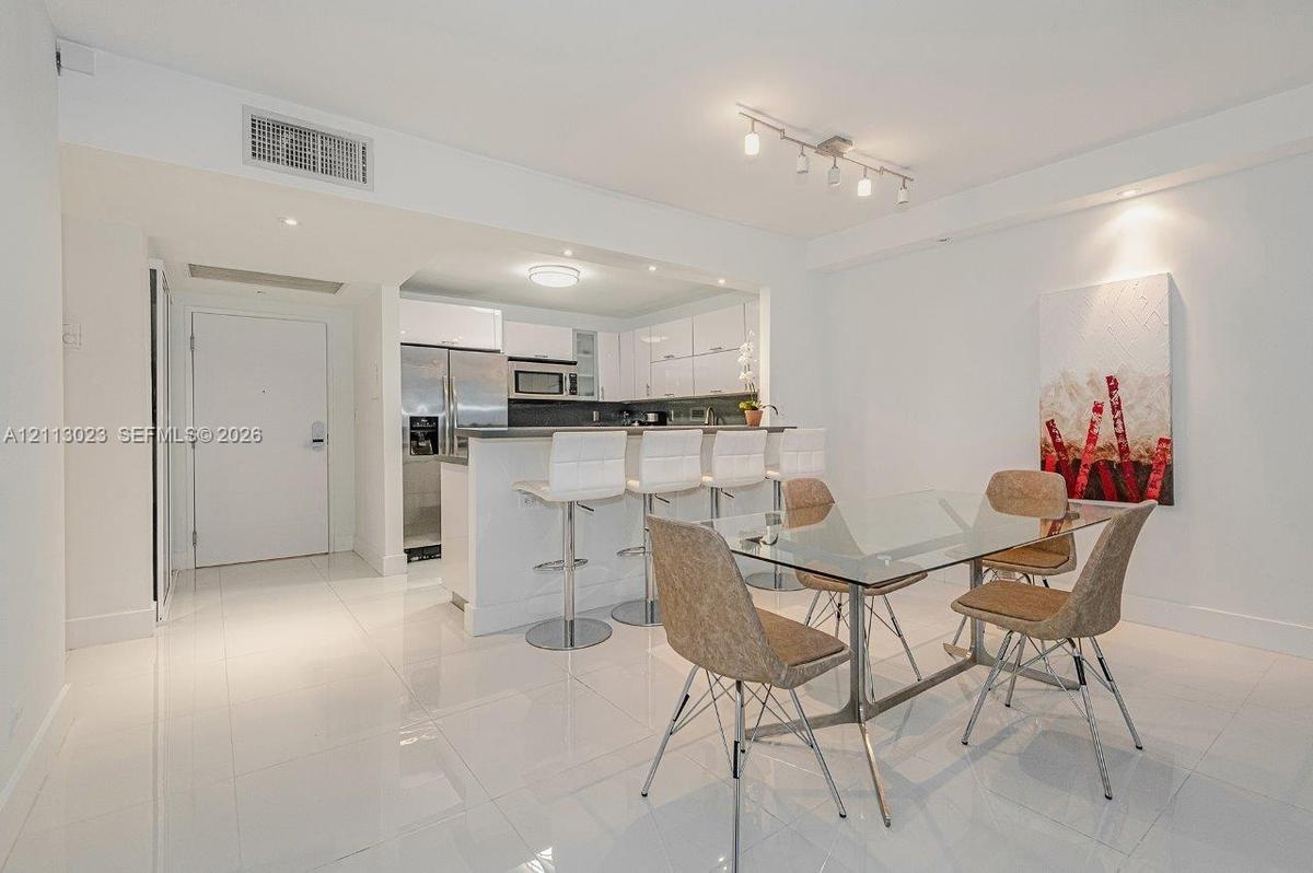 Open-concept kitchen featuring high-gloss cabinetry, stainless steel appliances, a breakfast bar, and polished white tile flooring