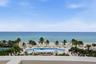 Oceanfront terrace featuring a concrete parapet, overlooking a resort-style swimming pool, lush palm trees, and sand beach
