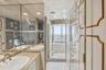 Bathroom featuring a stone-topped dual vanity with integrated sinks, floor-to-ceiling mirrors, tile wall detailing, a jetted soaking tub, and custom p
