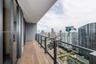 Covered balcony featuring wood-finish flooring, glass panel railing, and metal framing with a backdrop of urban architecture