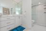 Bathroom featuring a glossy white vanity with a rectangular vessel sink, quartz countertop, full-height wall mirror, and a glass-enclosed shower with 