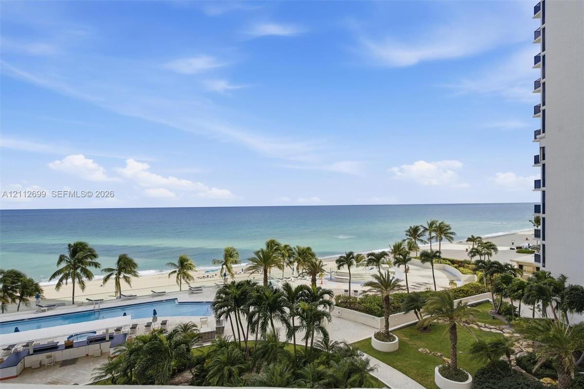 Elevated perspective featuring direct oceanfront access, a sprawling swimming pool with surrounding terrace, landscaped grounds with mature palms, and