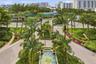 Landscaped motor court featuring a central tiered fountain, paver stone driveway, mature palm trees, and manicured tropical gardens