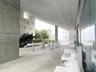 Expansive covered terrace featuring exposed concrete structural elements, floor-to-ceiling glass paneling, and integrated landscape planters