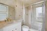 Stone-tiled bathroom featuring a vanity with a drop-in sink, gold-toned hardware, large wall-mounted mirror, and a walk-in shower with glass enclosure