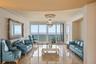 Polished stone flooring, expansive floor-to-ceiling glass panel doors, crown molding, and a crystal chandelier