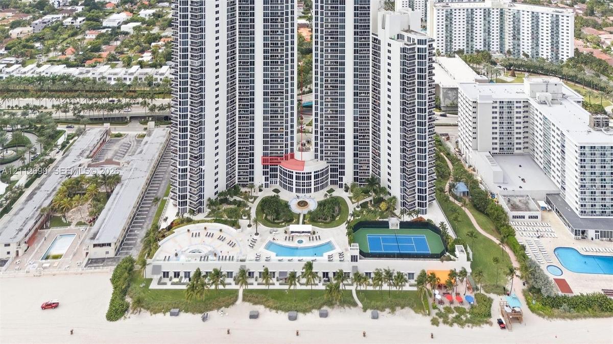 High-rise coastal property featuring an outdoor swimming pool, tennis court, landscaped grounds, and direct beach access