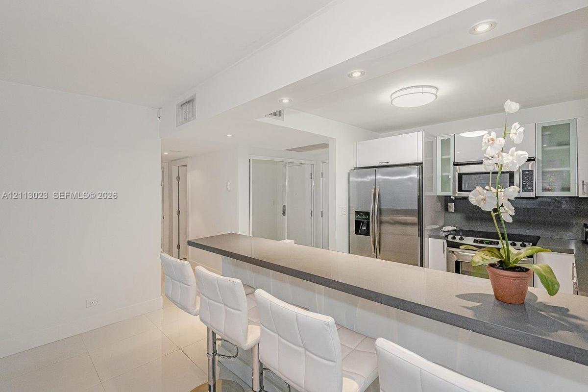 Kitchen featuring a stone-surface breakfast bar, white cabinetry, stainless steel appliances, and tile flooring, illuminated by recessed lighting