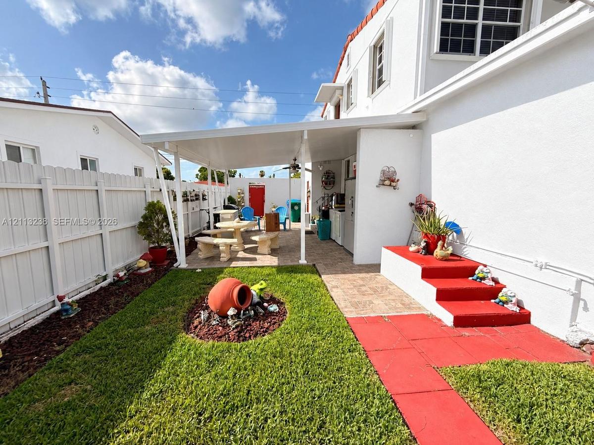 Enclosed backyard featuring a covered patio, paved hardscaping, a manicured lawn, and perimeter vinyl fencing