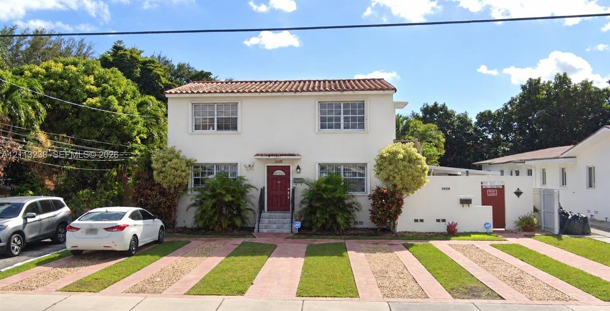 Two-story exterior featuring a terracotta tile roof, smooth stucco facade, multi-pane windows, and a paved ribbon driveway with integrated lawn strips