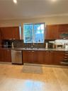 Kitchen featuring warm-toned wood cabinetry, natural stone countertops, a full-height stone backsplash, stainless steel dishwasher, and large-format t