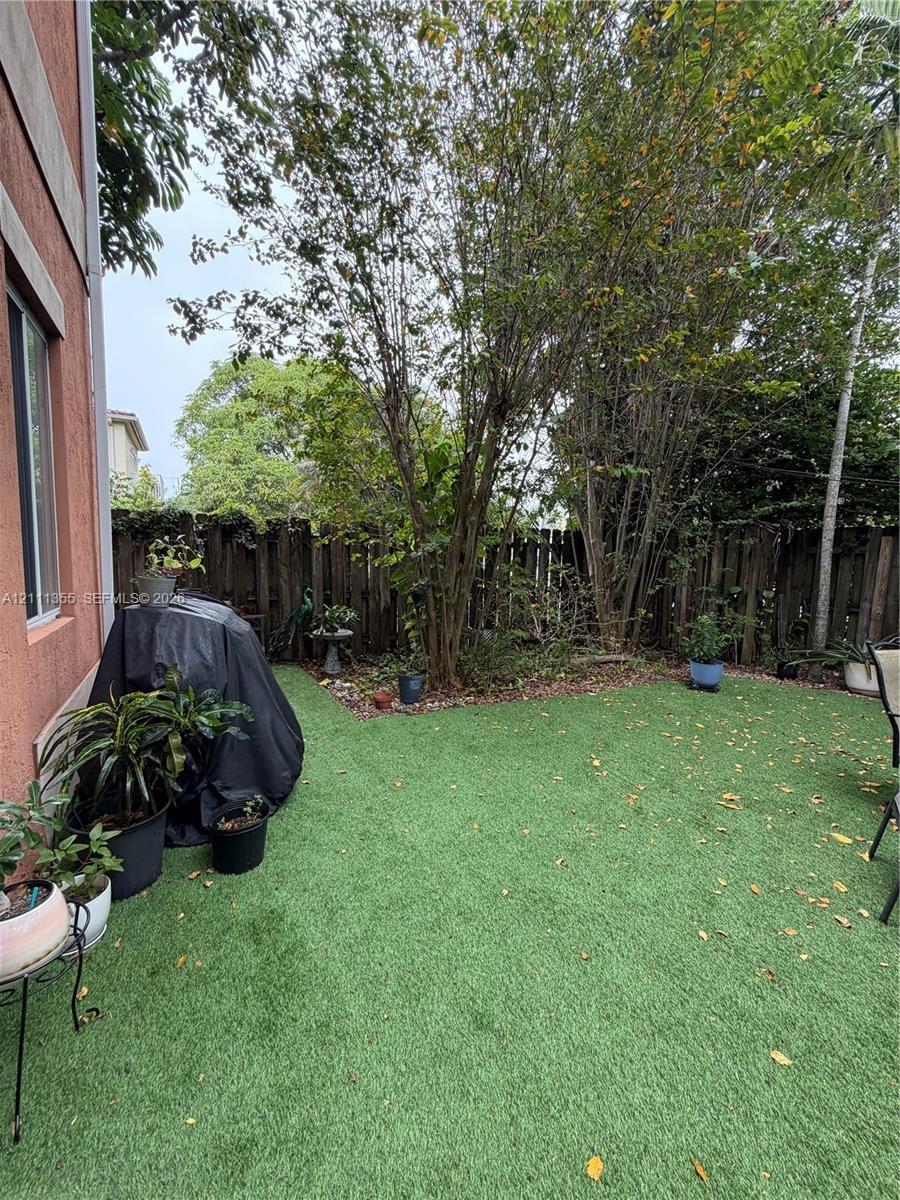 Enclosed backyard featuring synthetic turf, mature trees, and a wooden privacy fence