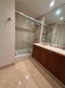 Bathroom featuring a vanity with wood-finish cabinetry, a light-toned stone-style countertop, a wall-spanning mirror, and a tub-shower combination enc