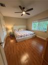 Room featuring wood-finish flooring, a multi-blade ceiling fan with integrated lighting, and a large window with a roller shade