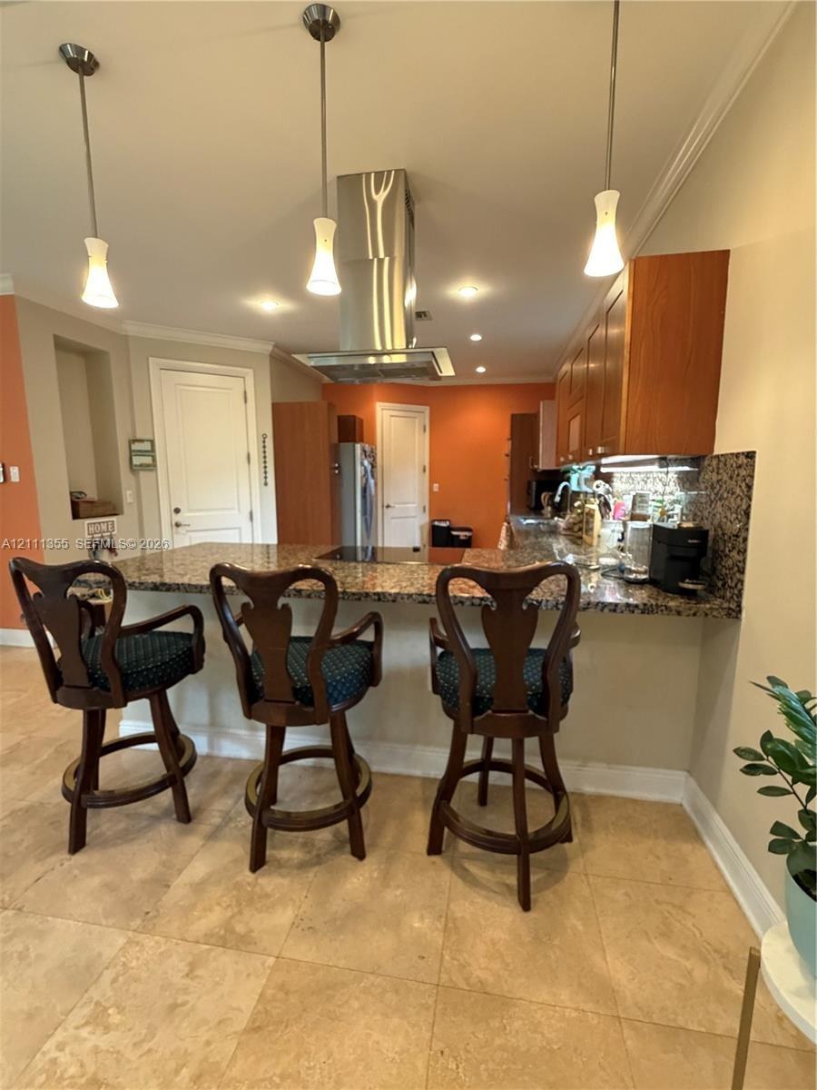 Kitchen featuring an expansive stone countertop, stainless steel ceiling-mounted vent hood, natural stone tile flooring, three pendant lights, and woo